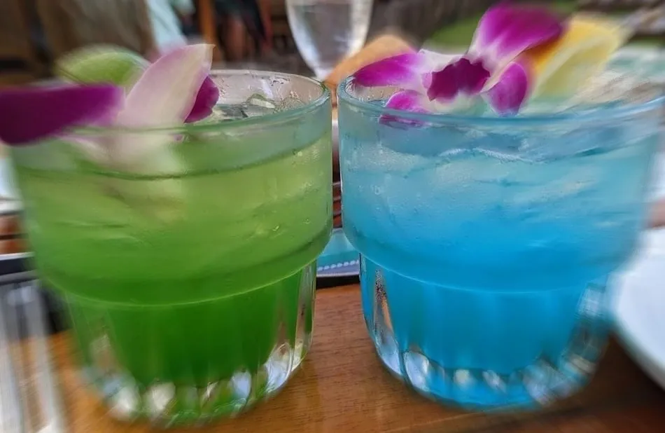 Two glasses of blue and green drinks on a table.