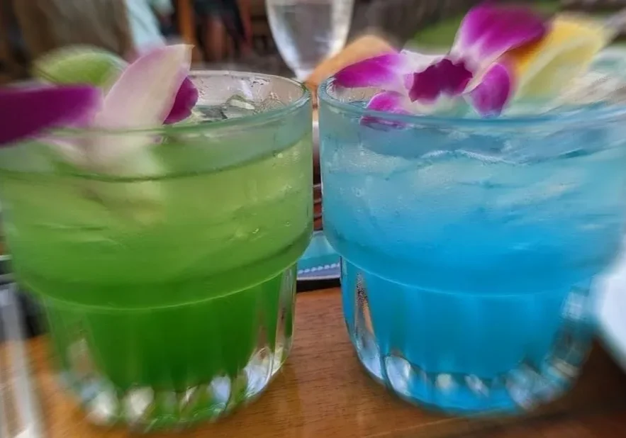 Two glasses of blue and green drinks on a table.