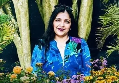 A woman in blue shirt standing next to flowers.