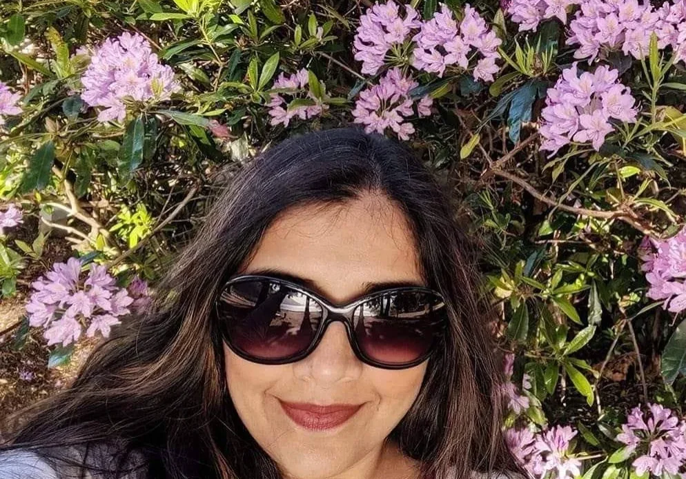 A woman in sunglasses standing next to some bushes.